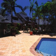 Exterior of house with brick cladding, dark grey arecales, backyard, estate, home, leisure, lighting, outdoor structure, palm tree, property, real estate, resort, swimming pool, tree, vacation, villa, walkway, black, orange