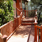 Exterior view of a wooden decking system and backyard, cottage, deck, handrail, home, house, outdoor structure, plant, property, real estate, tree, walkway, wood, yard, red