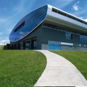 Exterior view of grey concrete clad stadium building architecture, building, corporate headquarters, daytime, facade, grass, headquarters, house, real estate, sky, structure, teal