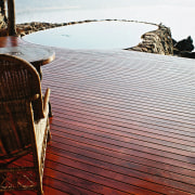 A view of some wooden decking. - A calm, horizon, reflection, sea, shore, sky, water, wood, white, red