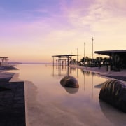 A view of some boulder-shaped artwork among the architecture, dawn, dusk, evening, horizon, morning, reflection, sea, sky, sunrise, sunset, water, orange, black