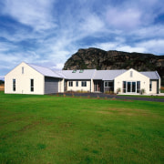 Exterior view of entire cream clad house with architecture, barn, cloud, cottage, estate, facade, farm, farmhouse, field, grass, grassland, home, house, land lot, landscape, lawn, pasture, property, real estate, residential area, roof, rural area, siding, sky, teal, green