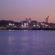 Distant view of Port of Auckland complex, showing body of water, calm, city, cityscape, dawn, downtown, dusk, evening, horizon, night, reflection, river, sea, sky, skyline, sunset, water, waterway, purple
