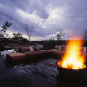 the outdoor seating area features an open fire backyard, campfire, evening, fire, heat, landscape, lighting, reflection, sky, sunlight, tree, water, water feature, black, purple