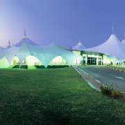 Exterior view of building featuring large canopy structure architecture, grass, landmark, plant, sky, structure, tree, blue