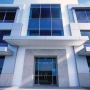 Exterior view of building lobby entrance with expansive apartment, architecture, building, commercial building, condominium, corporate headquarters, daylighting, daytime, elevation, facade, glass, headquarters, home, house, property, real estate, residential area, sky, window, gray, blue