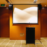 Function room with black podium, white screen and display device, flooring, furniture, interior design, projection screen, room, brown