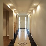 Long hallway with wall sconce luminaries casting pools apartment, architecture, ceiling, daylighting, floor, flooring, hall, interior design, light, lighting, lobby, real estate, wall, brown