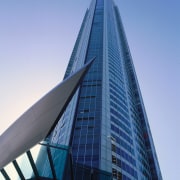 View of tall A1 apartment tower showing glass architecture, building, city, commercial building, condominium, corporate headquarters, daytime, headquarters, landmark, metropolis, metropolitan area, sky, skyscraper, tower, tower block, urban area, teal, blue