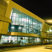 Exterior view of airport building showing extensive glazing. architecture, building, commercial building, corporate headquarters, daylighting, facade, metropolitan area, mixed use, night, yellow, brown