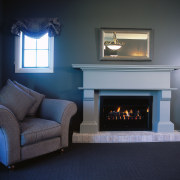 Fireplace with white surround, and large armchair. fireplace, furniture, hearth, home, home appliance, interior design, living room, wall, wood burning stove, black, gray