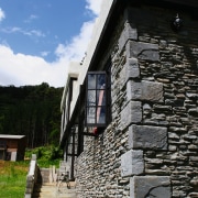 View of exterior of home clad in stone. building, cottage, facade, house, sky, stone wall, wall, window, black, gray