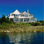 view of this cape cod home situated on building, cottage, estate, facade, home, house, lake, mansion, property, real estate, reflection, sea, sky, tree, water, waterway, blue