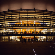 An exterior view of the building. - An architecture, building, city, corporate headquarters, darkness, evening, facade, landmark, light, lighting, metropolis, metropolitan area, night, reflection, sky, sport venue, stadium, structure, urban area, black, brown