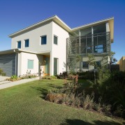 Exterior view of this beach house nestled amongst apartment, architecture, building, cottage, estate, facade, grass, home, house, property, real estate, residential area, sky, villa, window, brown, blue