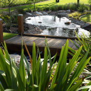 View of this timber boardwalk bridge crossing the backyard, flower, garden, grass, landscape, landscaping, outdoor structure, plant, pond, water, water feature, brown