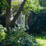 An exterior view of the house and its backyard, flora, flower, garden, grass, house, landscape, lawn, leaf, outdoor structure, plant, shrub, spring, sunlight, tree, vegetation, yard, black, green