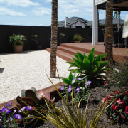 View of this outdoor enertainment area featuring landscaped arecales, backyard, courtyard, flora, flower, garden, home, house, landscape, landscaping, outdoor structure, plant, property, real estate, walkway, yard, black, white