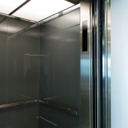 A view of the elevator lobby feauting glass elevator, glass, black, white