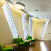 A view of the waiting area featuring polished architecture, ceiling, daylighting, floor, flooring, hardwood, house, interior design, light, light fixture, lighting, product design, room, wall, wood, brown, gray