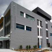 An exterior view of this building featuring metal architecture, building, commercial building, condominium, corporate headquarters, elevation, facade, headquarters, house, mixed use, real estate, residential area, gray, white