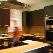 A view of this kitchen features cabinets by cabinetry, countertop, interior design, kitchen, light fixture, lighting, room, under cabinet lighting, brown