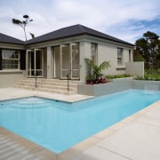 A view of a swimming pool built by backyard, estate, facade, home, house, property, real estate, residential area, swimming pool, villa, window, gray