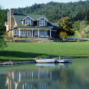 An exterior view of this traditional masonry home bank, canal, cottage, estate, farmhouse, home, house, lake, landscape, pond, property, real estate, reflection, reservoir, tree, water, waterway, green