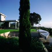 An exterior view of this house designed by architecture, backyard, estate, facade, grass, home, house, landscaping, plant, property, real estate, residential area, sky, tree, villa, black, teal