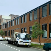 A view of this 1970s masonry warehouse with apartment, architecture, building, car, downtown, facade, family car, home, house, land vehicle, metropolitan area, mixed use, neighbourhood, property, residential area, sedan, town, transport, vehicle, brown