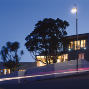 An exterior view of this modern urban home architecture, building, corporate headquarters, daytime, dusk, evening, facade, home, house, light, lighting, night, plant, residential area, sky, street light, tree, blue