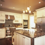 Underneath the cooktop are open stainless steel shelves, cabinetry, ceiling, countertop, cuisine classique, floor, flooring, hardwood, interior design, kitchen, lighting, room, under cabinet lighting, wood flooring, orange