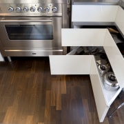 View of kitchen and living area designed by countertop, floor, flooring, hardwood, home appliance, kitchen, kitchen stove, wood, wood flooring, gray, brown