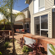 An exterior of this house featuring Merbau decking, backyard, cottage, deck, estate, facade, home, house, outdoor structure, property, real estate, residential area, siding, window, yard, brown