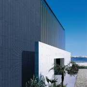 The layered facade of this oceanfront house in architecture, building, commercial building, corporate headquarters, daylighting, facade, headquarters, house, real estate, reflection, sky, blue