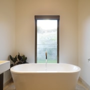 Bathroom, featuring freestanding tub beneath a window. bathroom, bathtub, daylighting, floor, interior design, plumbing fixture, room, window, orange, brown