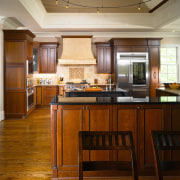 The oversized range hood connects tonally with adjacent cabinetry, ceiling, countertop, cuisine classique, floor, flooring, hardwood, interior design, kitchen, room, wood, wood flooring, brown