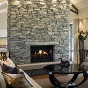 The central schist fireplace is left unadorned, as fireplace, hearth, home, interior design, living room, room, gray