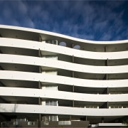 Exterior view of the Flow Apartments which sit apartment, architecture, building, commercial building, condominium, corporate headquarters, daytime, facade, headquarters, line, metropolis, metropolitan area, mixed use, real estate, residential area, sky, tower block, urban area, white, black, blue