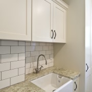 View of laundry, featuring a white butler's sink, bathroom, bathroom accessory, bathroom cabinet, cabinetry, countertop, floor, flooring, home, interior design, kitchen, laundry room, room, sink, tile, gray