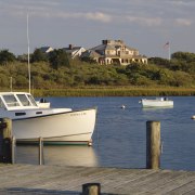 Exterior view of cottage beyond the water way. boat, boating, body of water, coast, coastal and oceanic landforms, dock, harbor, marina, ocean, recreation, sea, shore, sky, tree, vehicle, water, watercraft, waterway, gray