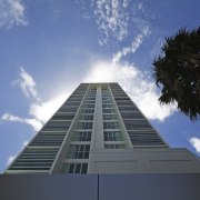 Exterior view of the Proximity Apartments which were architecture, arecales, building, cloud, condominium, daytime, facade, landmark, metropolitan area, palm tree, sky, skyscraper, symmetry, tree, teal, black