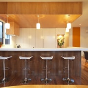 View of kitchen area featuring an island with cabinetry, ceiling, countertop, flooring, hardwood, home, interior design, kitchen, lighting, real estate, room, under cabinet lighting, wood, brown, orange