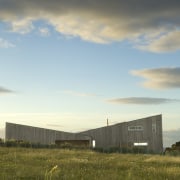 Exterior view of residence which features a monopitched architecture, cloud, dawn, energy, evening, farm, field, grass, grassland, home, horizon, house, landscape, meteorological phenomenon, morning, plain, prairie, real estate, rural area, sky, sunlight, gray