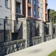 View of the stone wall with metal sections building, facade, fence, handrail, home fencing, house, iron, neighbourhood, outdoor structure, property, real estate, residential area, walkway, wall, black, gray