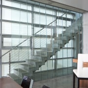 View of living space and staircase featuring vertical architecture, daylighting, glass, handrail, interior design, stairs, window, gray