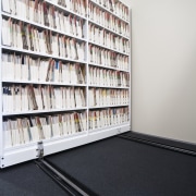 View of adjustable storage shelves with lockable handwheels. bookcase, floor, flooring, library, public library, shelf, shelving, white, black