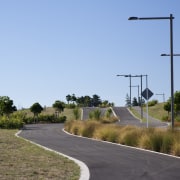 View of surrounding landscape of a energy-efficient development. asphalt, field, grass, infrastructure, land lot, lane, road, road surface, rural area, sky, street light, tree, teal