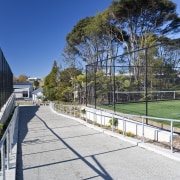 Exterior view of a concrete pathway at Albany architecture, area, estate, fence, grass, house, landscape, outdoor structure, park, plant, public space, real estate, recreation, residential area, sky, sport venue, structure, tree, walkway, white
