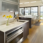 View of contemporary kitchen which features island, stainless cabinetry, countertop, floor, flooring, interior design, kitchen, wood flooring, gray, brown